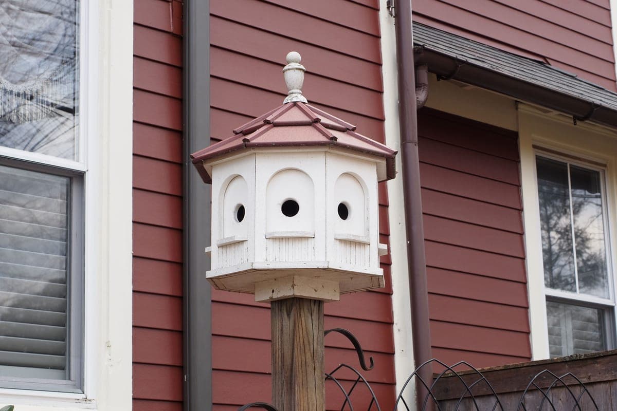A vintage birdhouse mounted on a post against a red wall