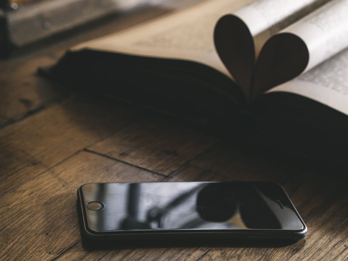 A smartphone resting beside an open book on a wooden table
