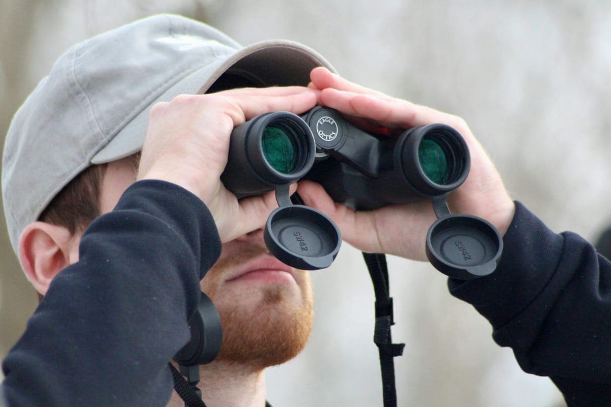 A man in a cap looking through binoculars outdoors