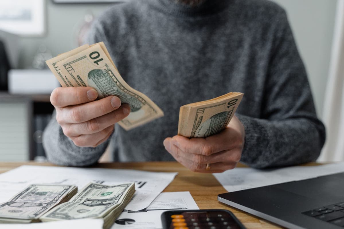 Hands counting cash beside a calculator and paperwork
