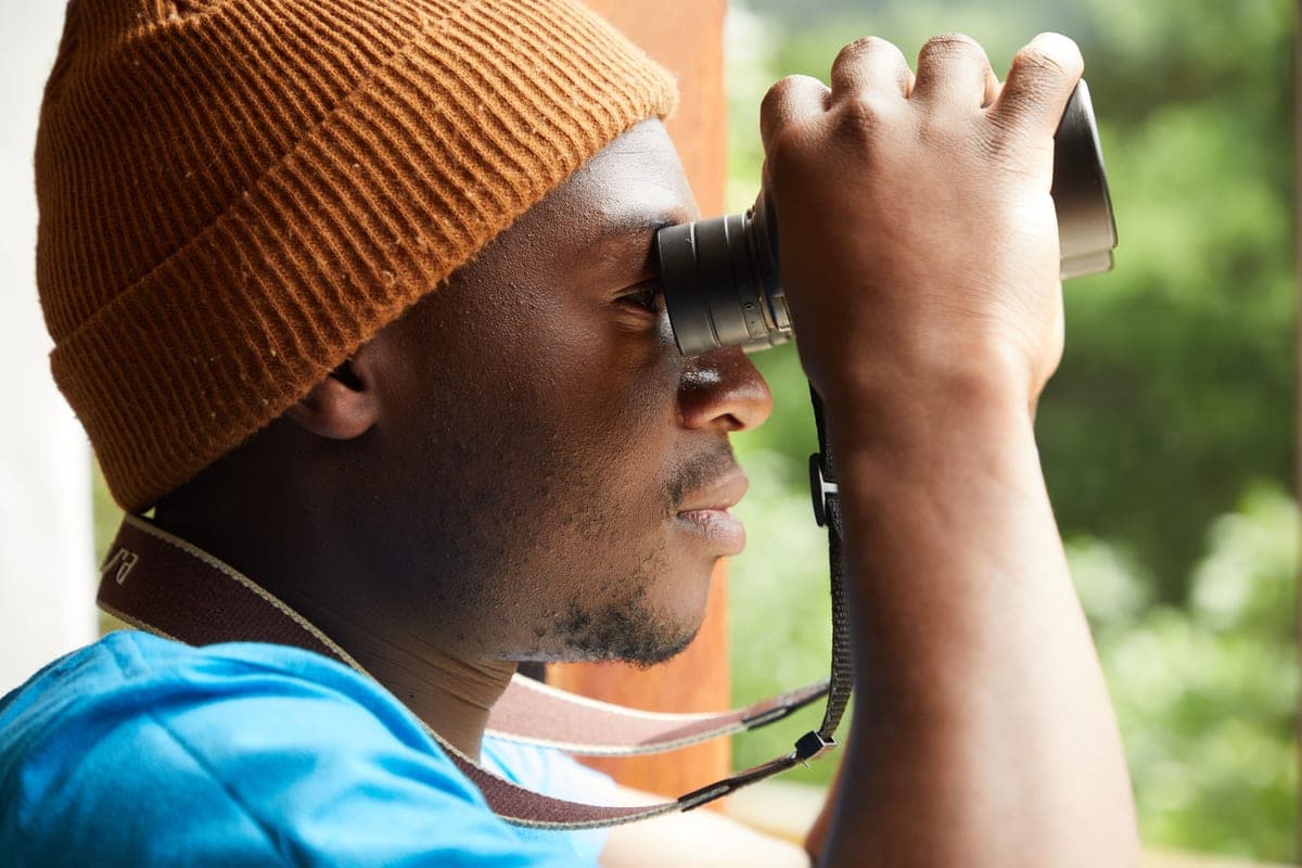 A man in a hat looking through binoculars from an open window