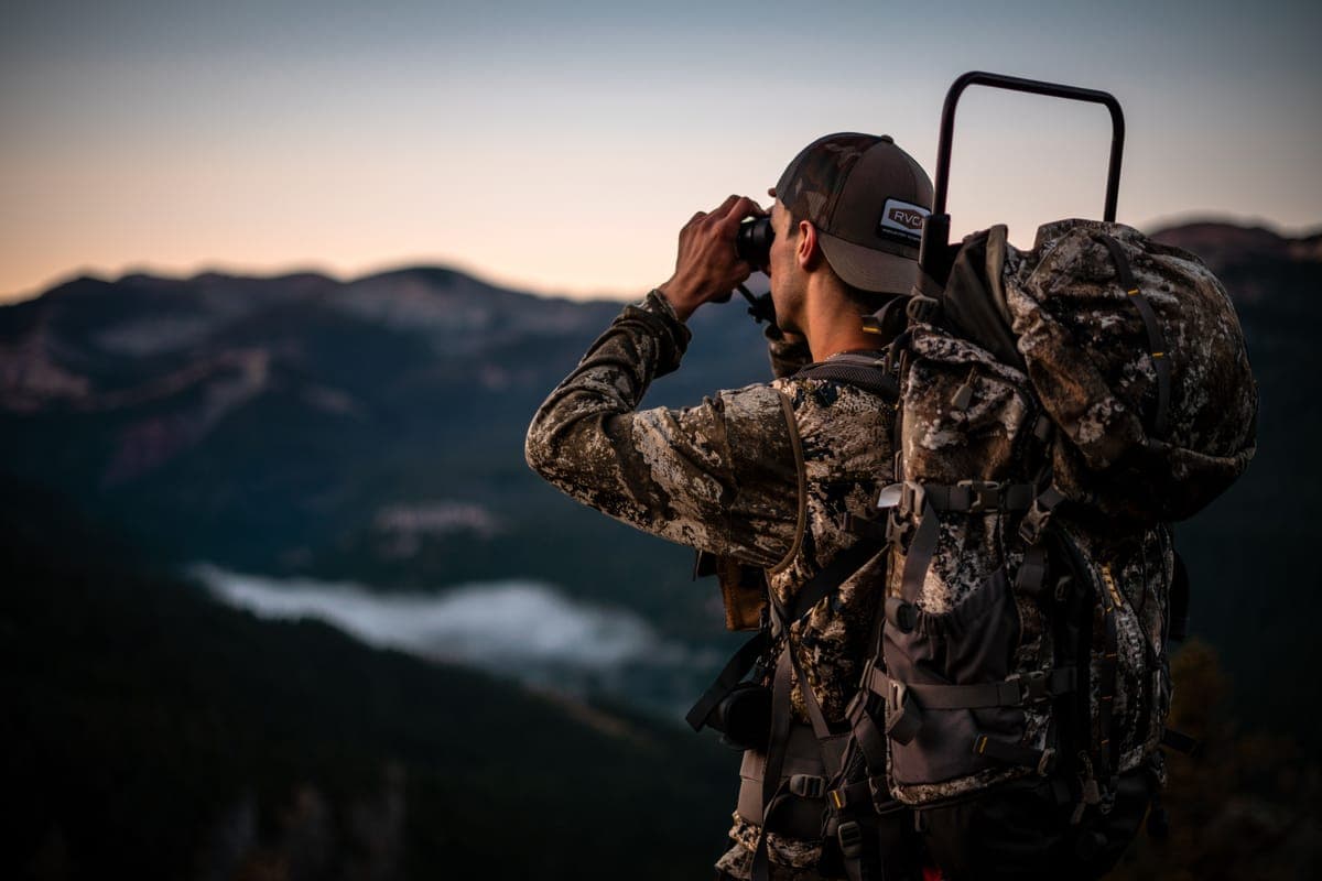 A hiker with a backpack using binoculars in a mountain landscape