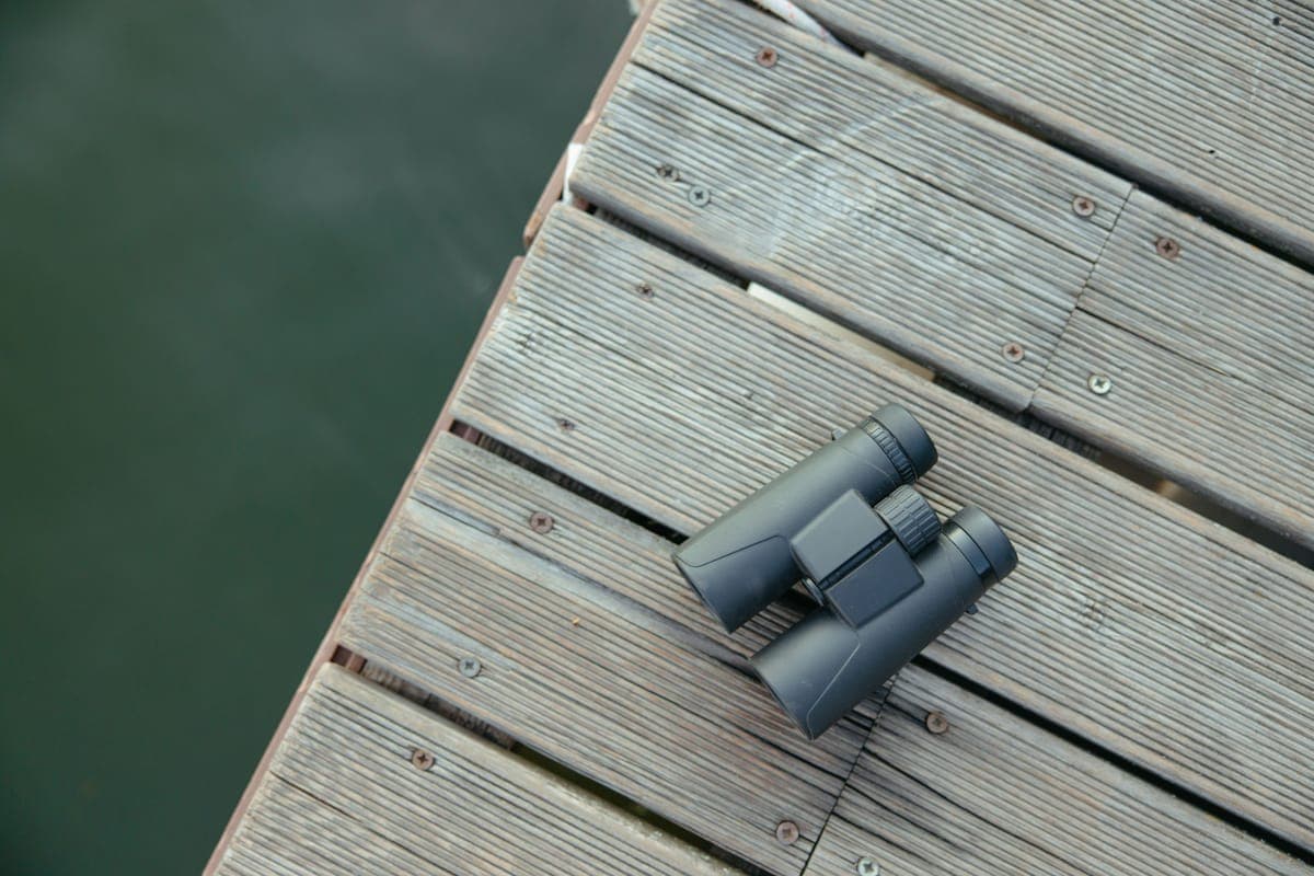 Black binoculars resting on a wooden dock above water