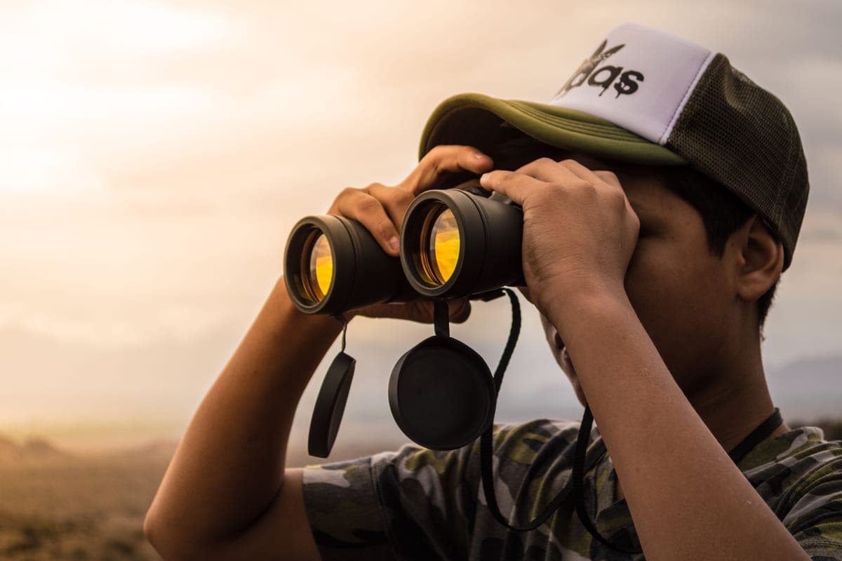 A man in a cap using binoculars outdoors on a bright day