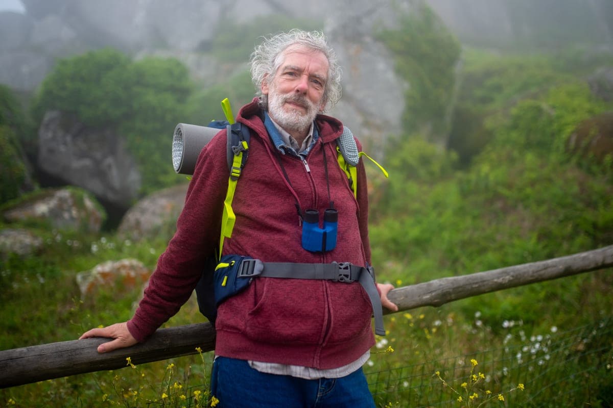 A hiker with a backpack and binoculars on a misty upland trail